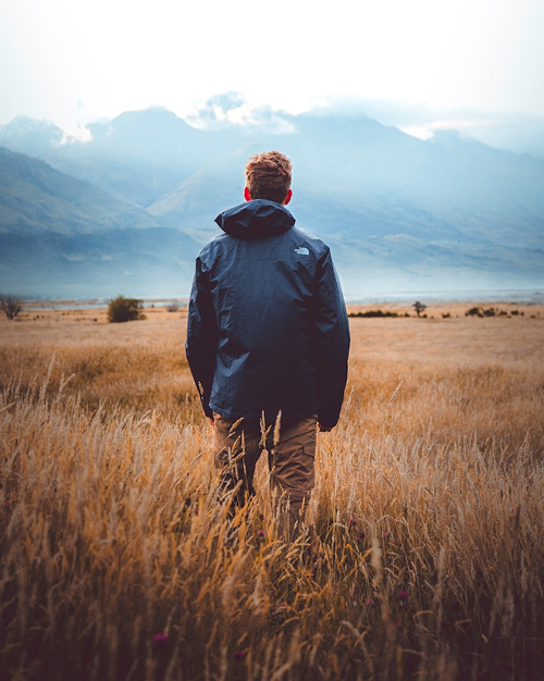a young man in an open field staring at the mountain